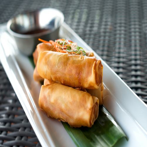 Vegetable fried spring rolls served with bittersweet sauce on wicker table close up.