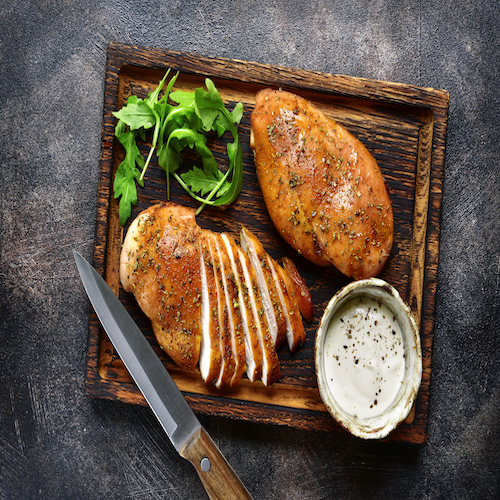 Grilled chicken breast in a sweet and sour marinade with yogurt sauce on a wooden cutting board.Top view.