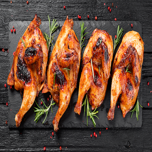 Halves of appetizing grilled juicy chicken with golden brown crust served with lemon slices,barbeque  sauce and rosemary.