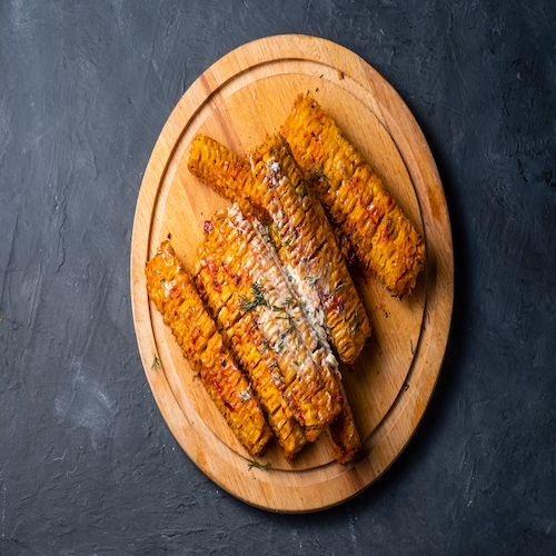 Corn on the cob grilled with spices and butter on a wooden round board. Top view.