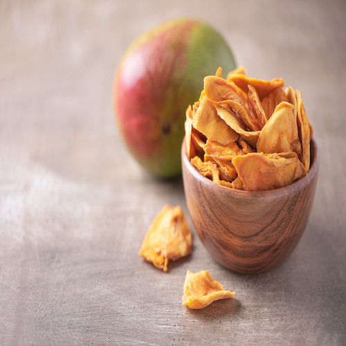Dried mango in wooden bowl and fresh mango fruit on wood textured background. Copy space. Superfood, vegan, vegetarian food concept. Macro of orange dried mango slices, selective focus. Healthy snack.