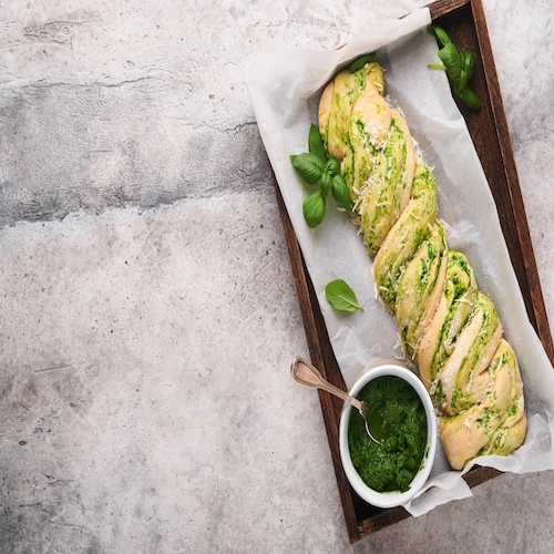 Braided wild garlic pesto brioche. Homemade raw or uncooked fresh pull apart bread with wild garlic pesto on wooden board on old grey background table. Italian bread. Copy space. Top view.