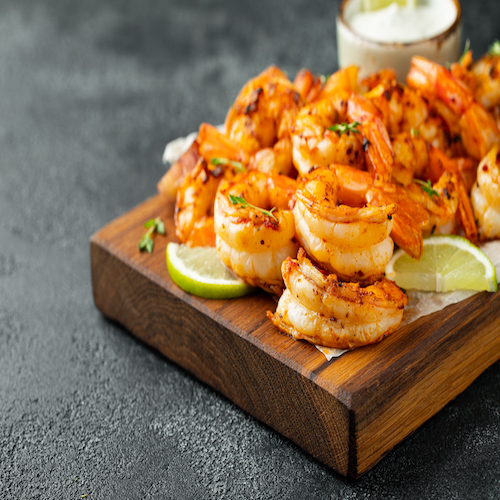 Grilled shrimps or prawns served with lime, garlic and white sauce on a dark concrete background. Seafood
