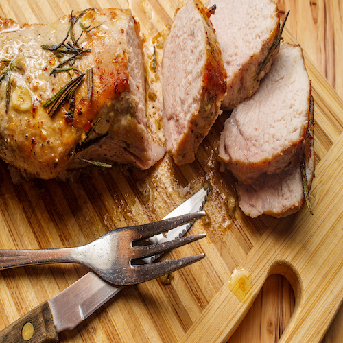 Sliced honey mustard roast pork tenderloin on wooden kitchen cutting board