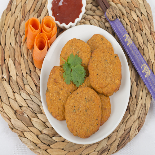Tod Man Pla - Thai fried fishcakes served with a bowl of sweet chili sauce and garnished with coriander leaves and sliced carrots.