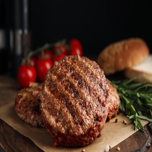 Tasty grilled hamburger patties with seasonings on wooden table, closeup