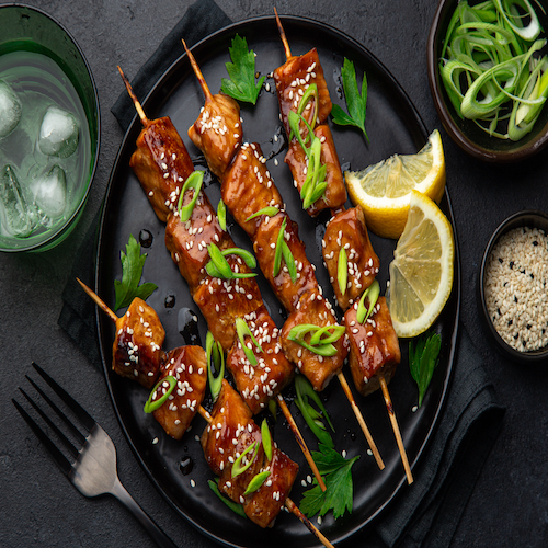Teriyaki salmon skewers on black plate, top view