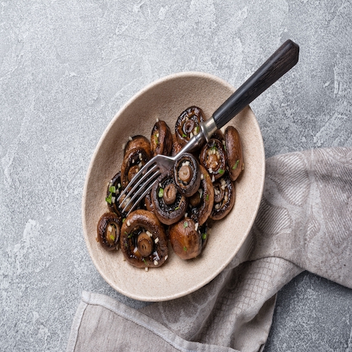 Top view of grilled champignon mushrooms in bowl with spice on grey concrete background