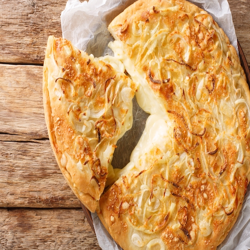 Fugazzeta Argentinian Stuffed Pizza is filled with a layer of mozzarella cheese with sliced onions and even more cheese on top closeup in the plate on the wooden table. Horizontal top view from above