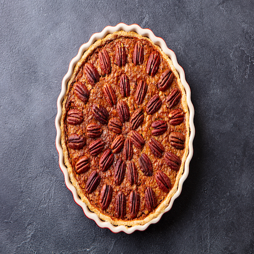 Pecan pie, tart in baking dish. Traditional festive Thanksgiving dessert. Dark background. Top view.