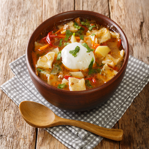 Delicious Pancutras or Pantrucas soup with vegetables, ground beef, noodles and poached egg close-up in a bowl on the table. horizontal
