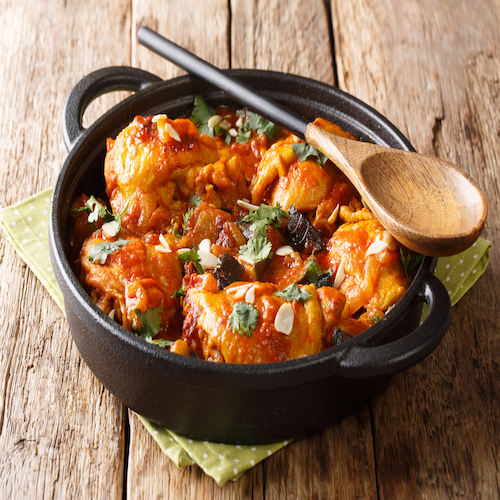 Moroccan recipe Chicken with eggplant, almonds with vegetable gravy close-up in a pan on the table. Traditional summer food.